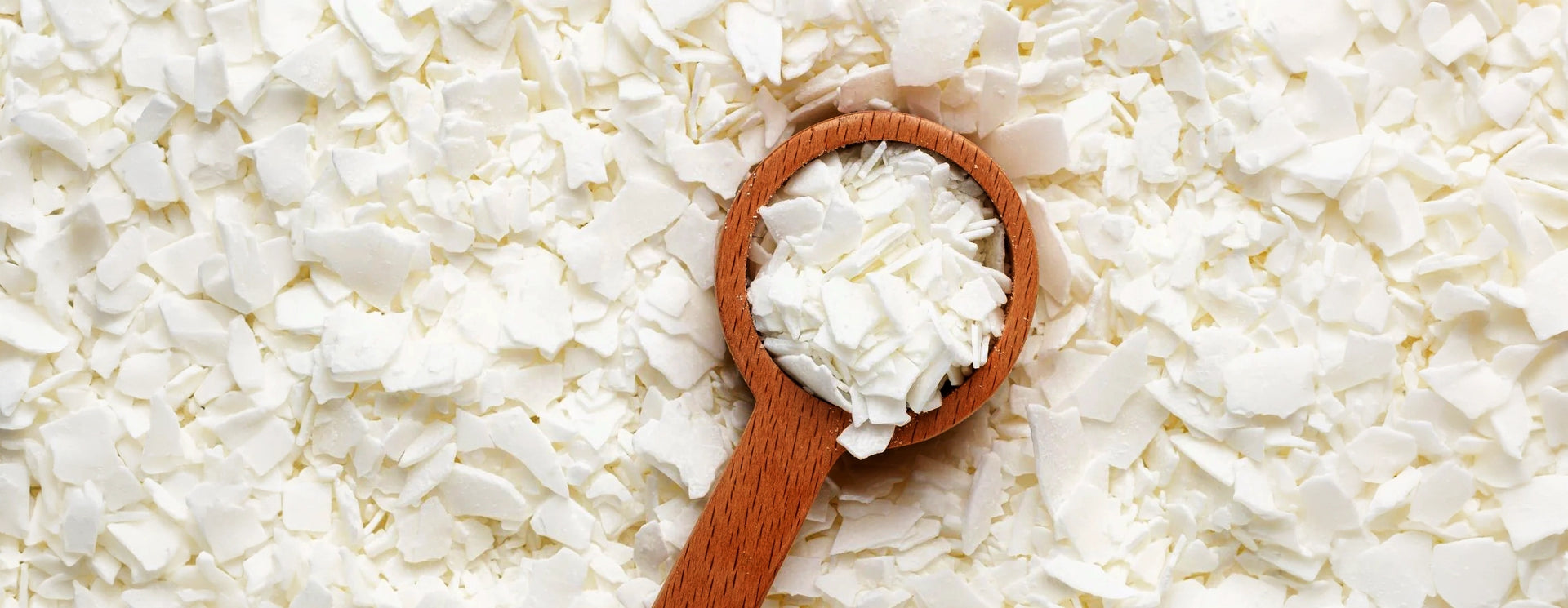 Weiße Sojawachs-Flocken auf hellem Untergrund mit Holzlöffel, pflanzliches Rohmaterial für vegane Kerzen