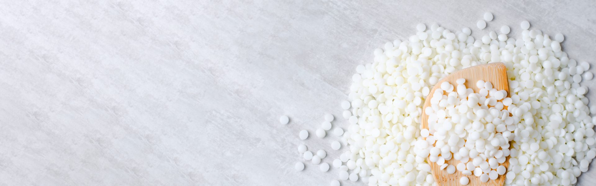 Weiße Sojawachs-Pellets auf hellem Marmoruntergrund mit Holzlöffel, veganes Rohmaterial für herzton Kerzen