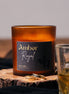 herzton Amber Royal Duftkerze im Bernsteinglas mit schwarzem Etikett und goldener Schrift, auf Holzscheibe mit Ringen