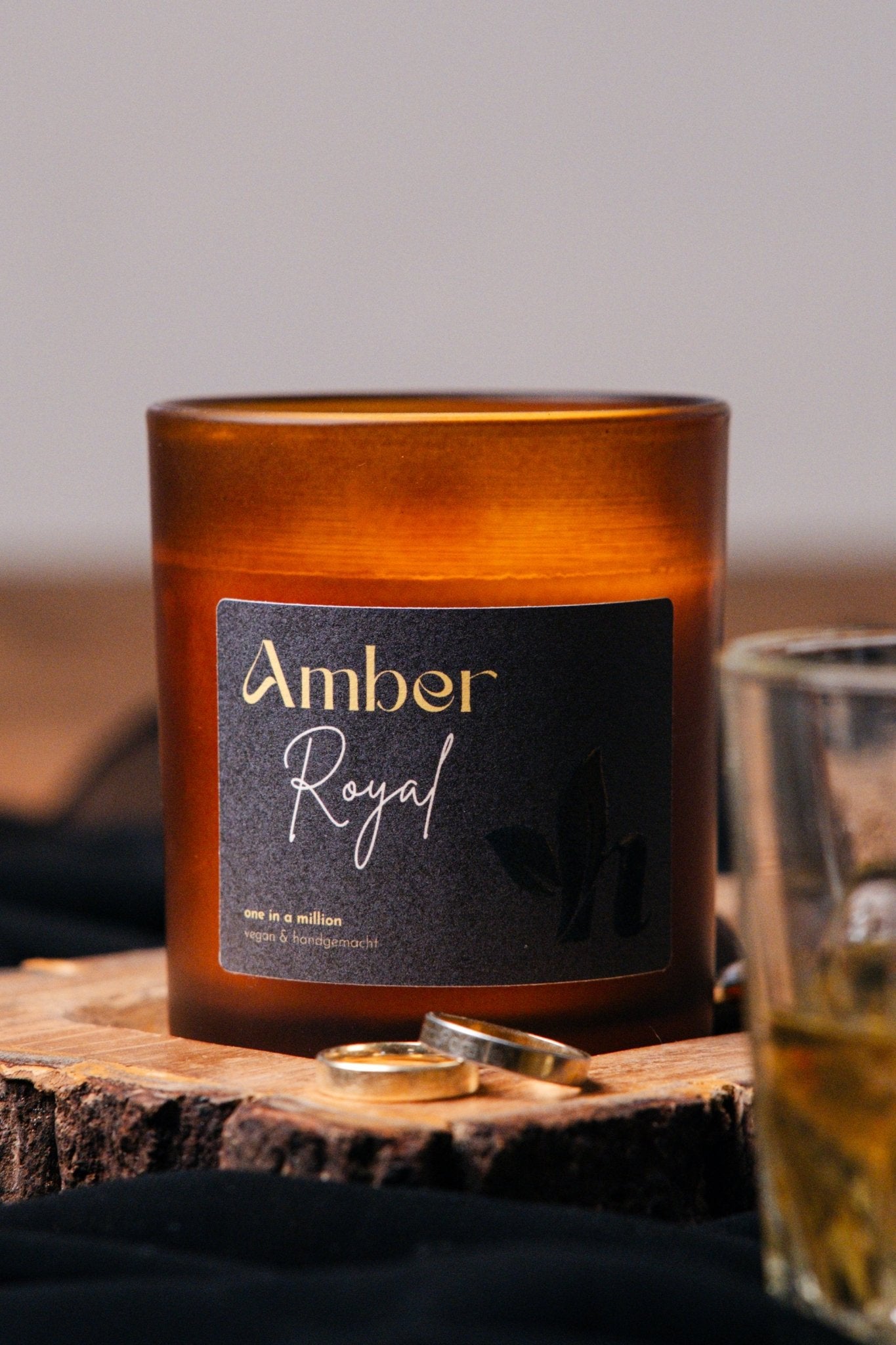 herzton Amber Royal Duftkerze im Bernsteinglas mit schwarzem Etikett und goldener Schrift, auf Holzscheibe mit Ringen