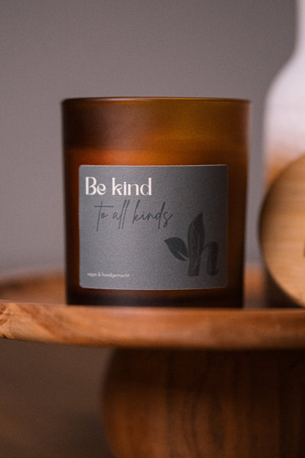 herzton Sojawachskerze im Bernsteinglas mit grauem Etikett und Aufschrift "Be kind to all kinds", auf Holztablett