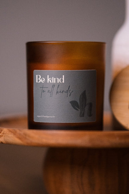 herzton Sojawachskerze im Bernsteinglas mit grauem Etikett und Aufschrift "Be kind to all kinds", auf Holztablett