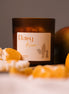 herzton Daisy Dream Duftkerze im Bernsteinglas mit Mango und Mandarine, Etikett auf grauem Hintergrund