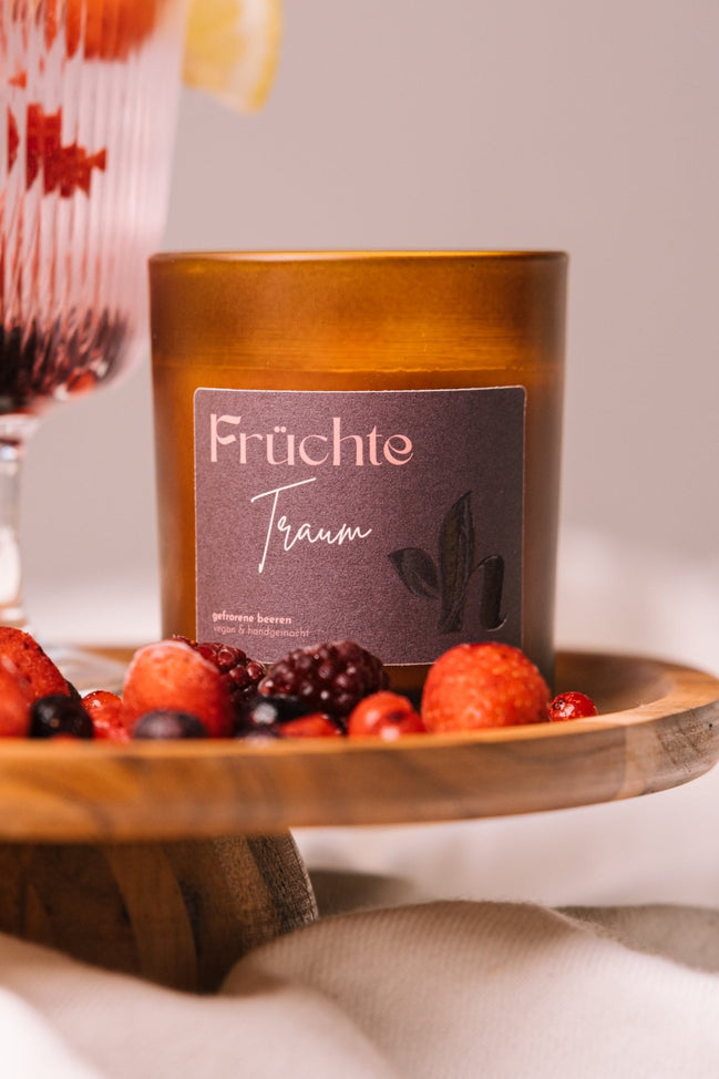 herzton Früchtetraum Duftkerze im Bernsteinglas mit dunkelrotem Etikett, auf Holztablett mit gemischten Beeren