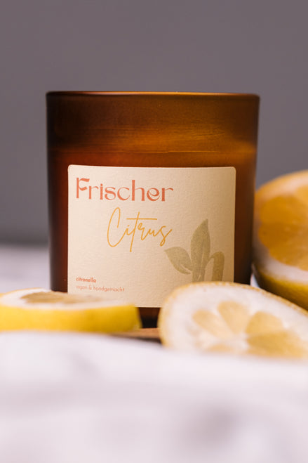 herzton Frischer Citrus Duftkerze im Bernsteinglas mit hellem Etikett, Zitronenscheiben als Dekoration