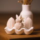Cremefarbene handgeformte Ostereier und Hase im weißen Keramik-Eierhalter, weiße Vase mit Trockenblumen dahinter