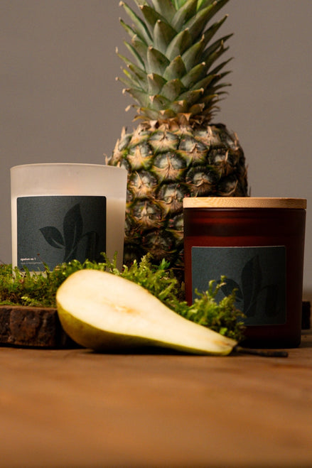 herzton Signature Kerze im Milchglas und Bernsteinglas nebeneinander, Ananas und Birne als Duft-Dekoration