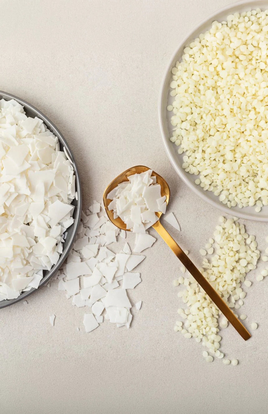 Sojawachs-Flocken und Granulat in Schalen mit goldenem Löffel, vegane Kerzenmaterialien auf hellem Grund
