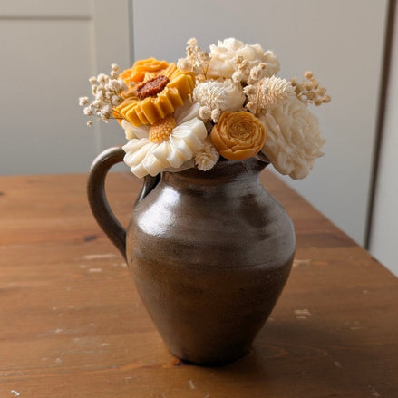 herzton Wachsblumenstrauß in braunem Vintage-Keramikkrug, Sojawachs-Blüten in Weiß und Gelb auf Holztisch